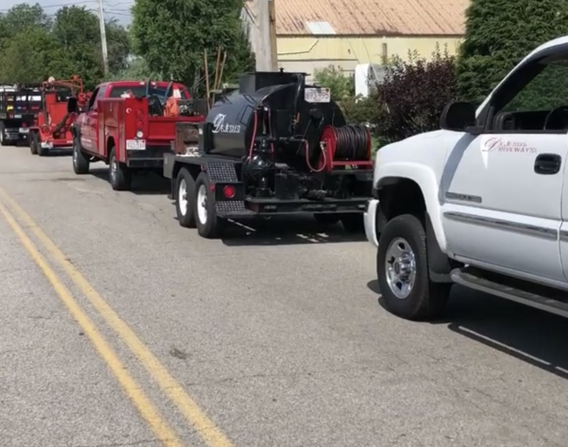 Red service truck, black sealcoating trailer and white pickup parked in a line along a road