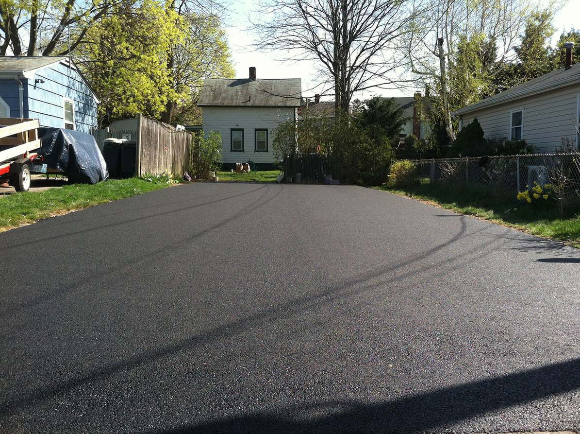 Wide freshly paved glossy black asphalt driveway between houses on a residential street