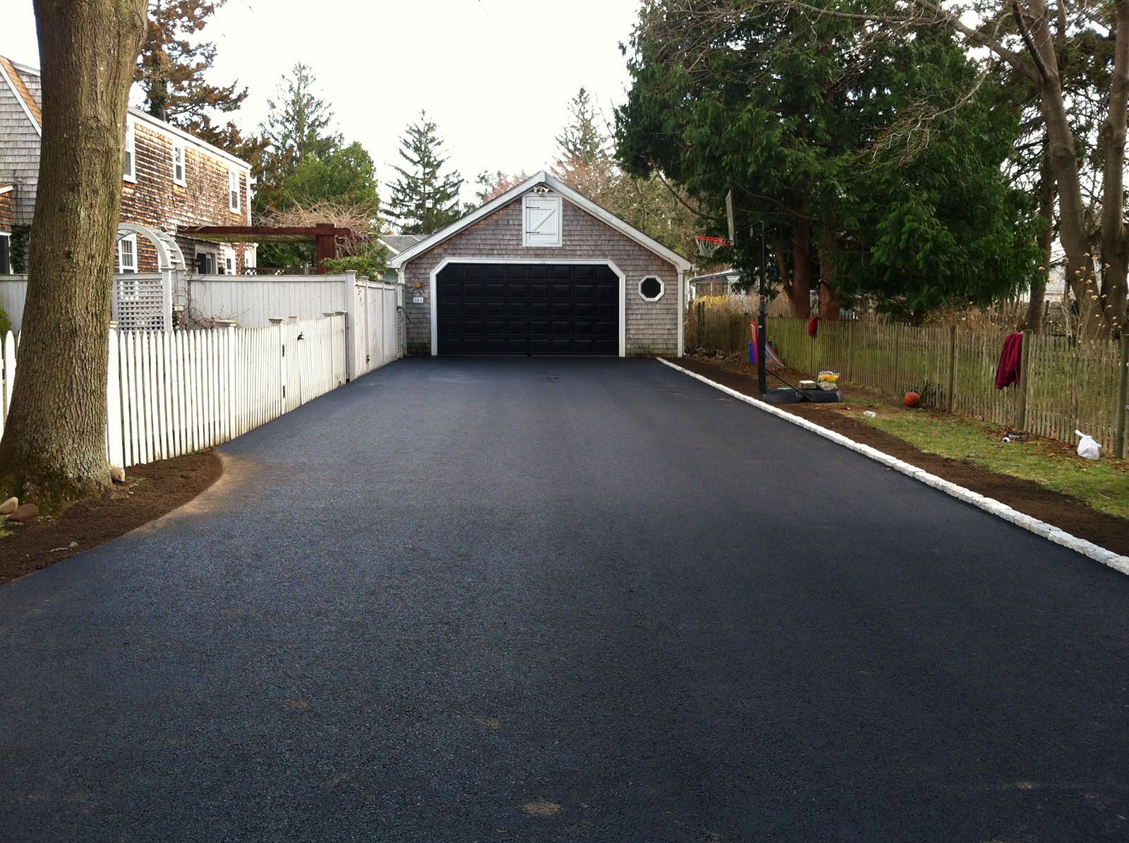 Long freshly paved black asphalt driveway with a white edge border leading to a barn-style garage with a black door