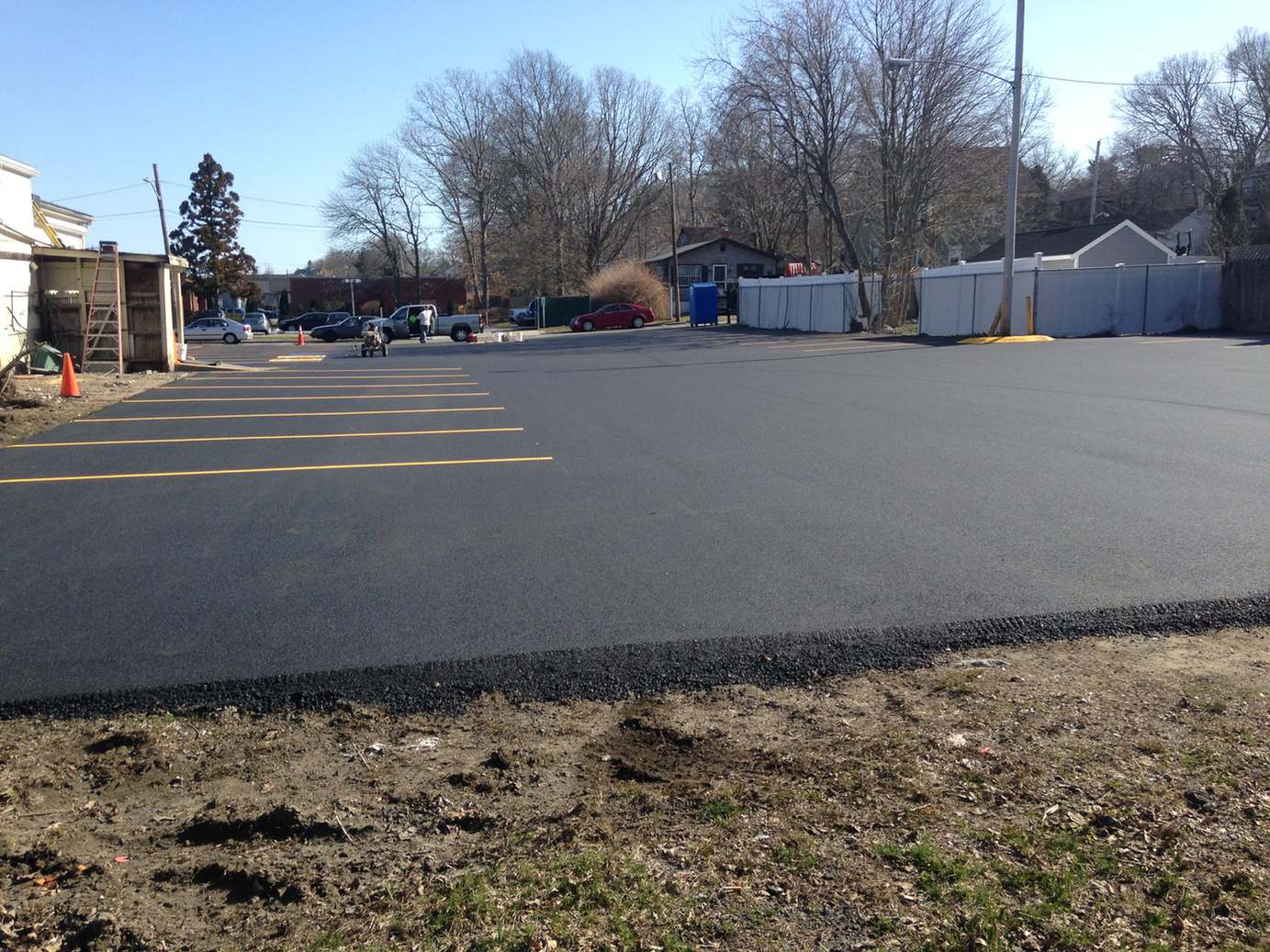 Newly paved asphalt parking lot with fresh yellow parking space lines painted along the left side